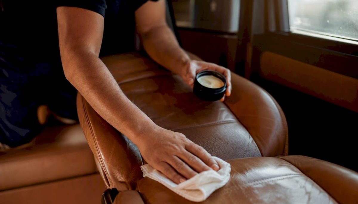 Hands applying enzymatic cleaner on leather car seat