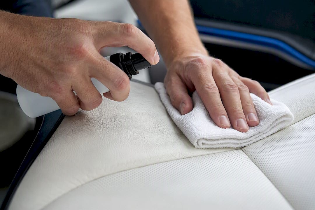 Hands applying odor treatment to leather car seat
